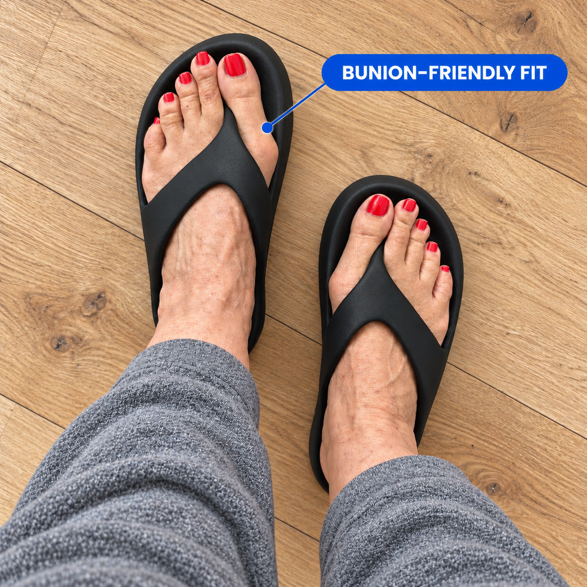 Top-down view of a person wearing black slide sandals on a wood floor, with one sandal highlighted by a blue callout reading “BUNION-FRIENDLY FIT.”.